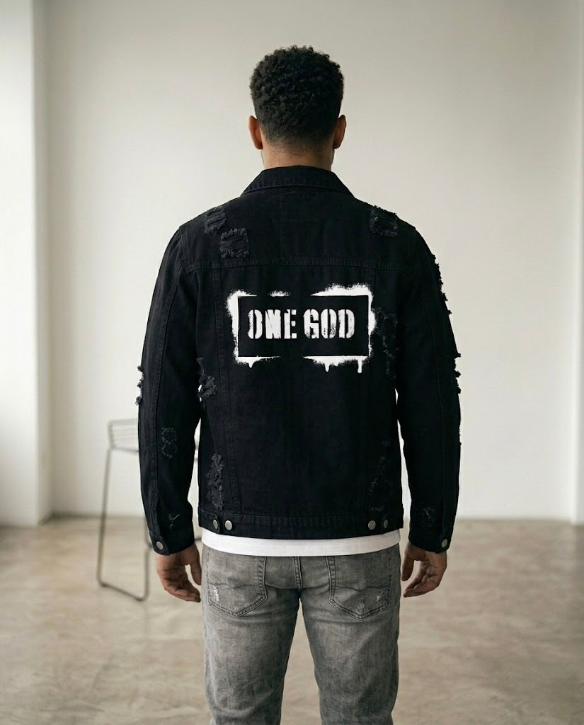 Person wearing a black denim jacket with 'ONE GOD' printed on the back in a minimal indoor setting.