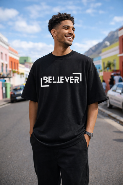 Model wearing the Halal Vibes BELIEVER oversized tee in a bright outdoor urban setting.