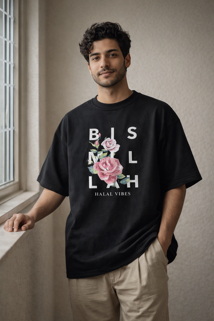 Man wearing a black t-shirt with floral design and bismillah  text in a room with a window.