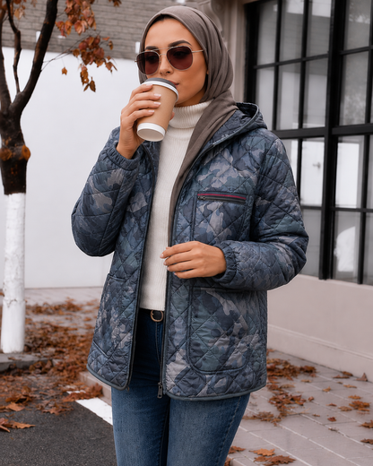 Woman in a blue quilted jacket drinking from a coffee cup outdoors.