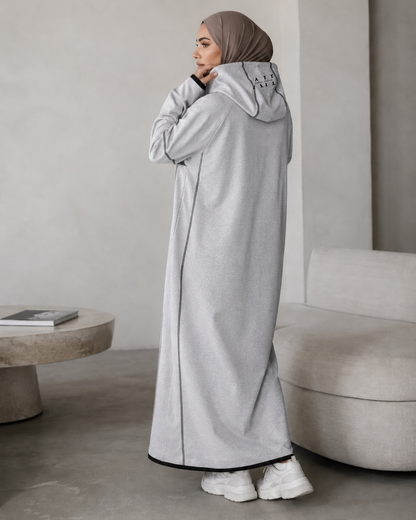 Full-length heather grey tech-fleece abaya with a black chest panel, hooded top with HV monogram, and waterproof black zippered pockets, lifestyle