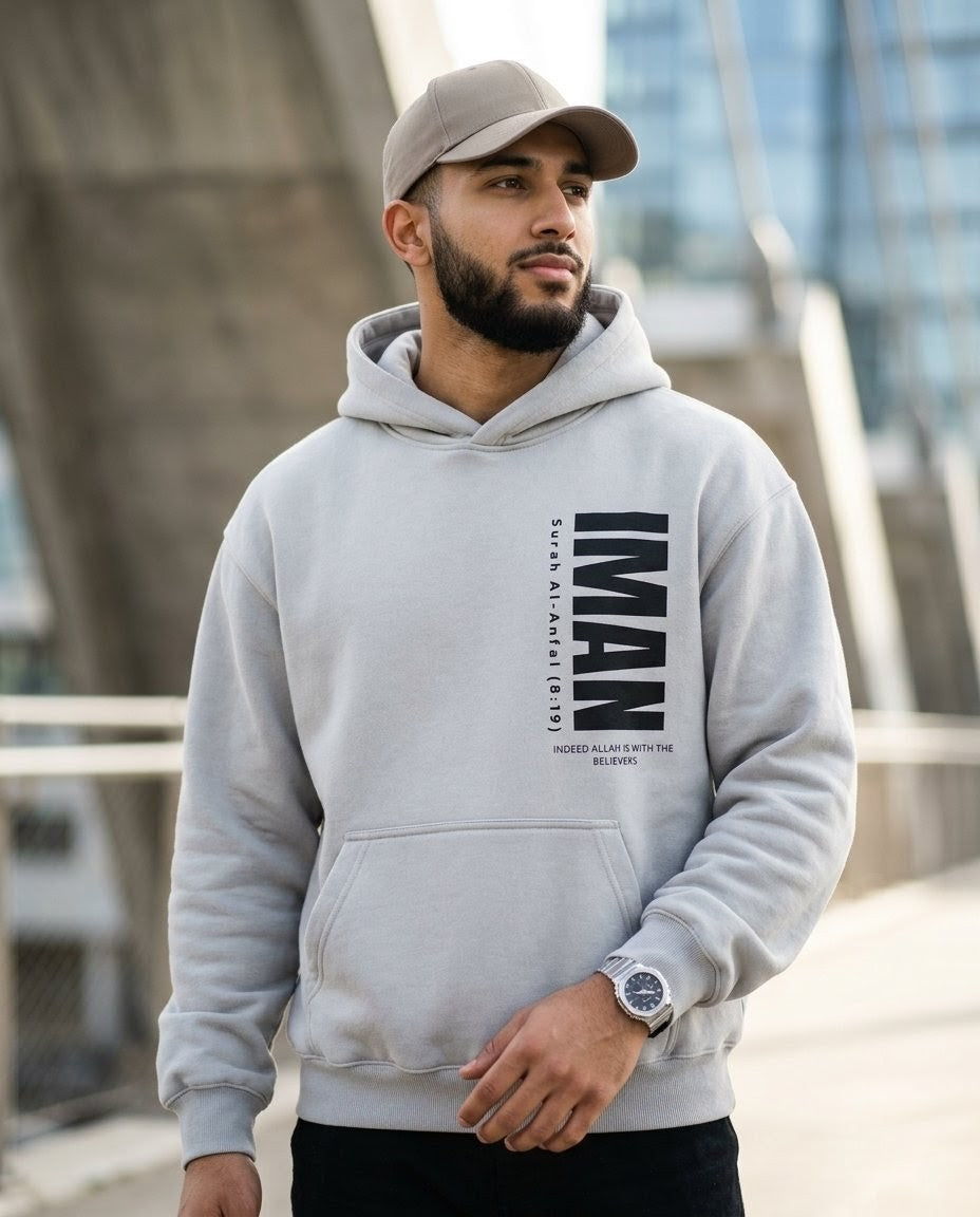 Man wearing a gray hoodie with text, standing outdoors with modern architecture in the background