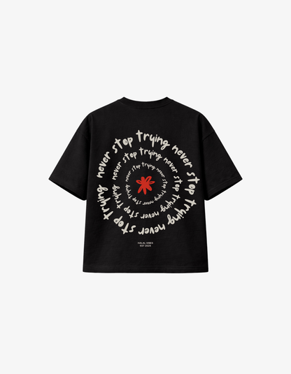 Back view of black streetwear tee featuring a white "Never Stop Trying" spiral typography and red flower.