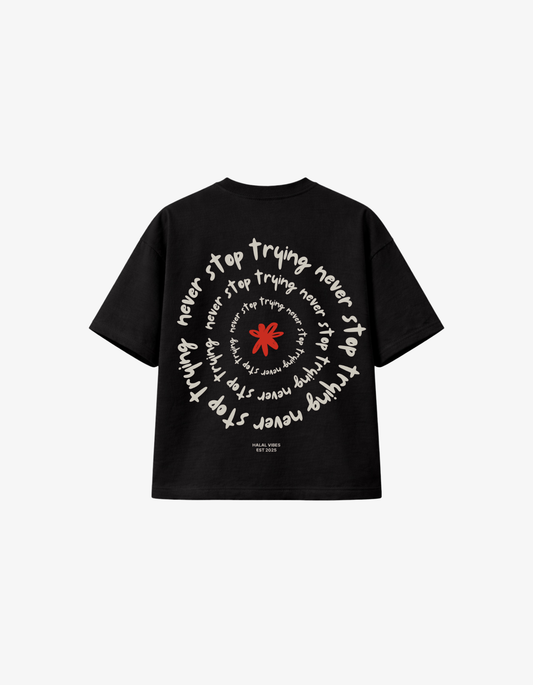 Back view of black streetwear tee featuring a white "Never Stop Trying" spiral typography and red flower.